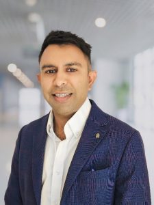 A photo of Neil Chavda, RPI Consultant. Neil is smiling and wearing a white shirt with a blue jacket. He has dark hair.